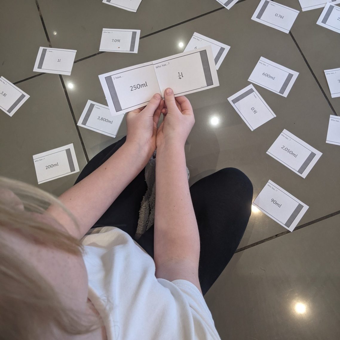 A child sits on the floor surrounded by scattered cards, holding one card in their hands.