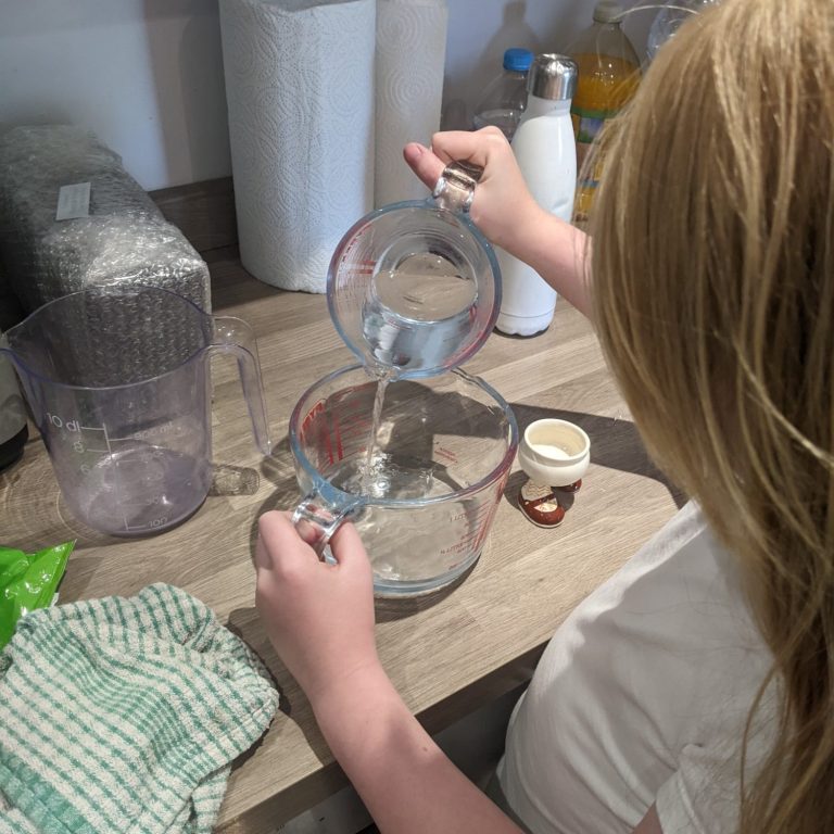 A child pouring water into a measuring jug on a kitchen counter.